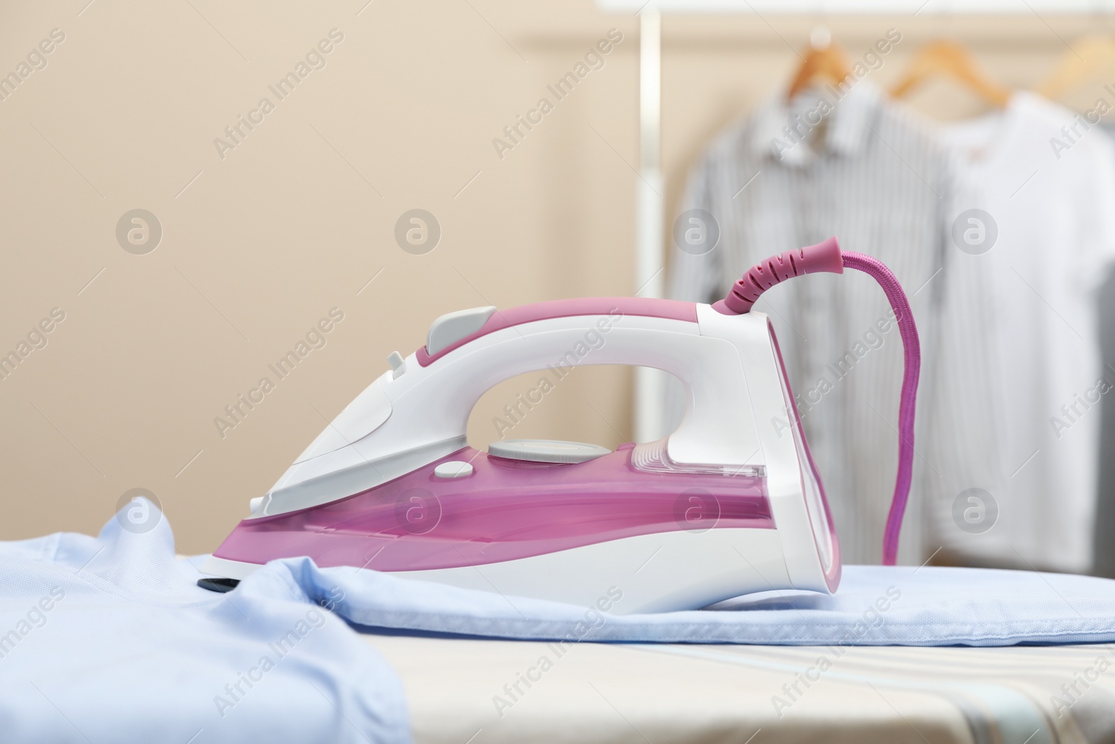 Photo of New modern iron and clean shirt on board against beige background. Laundry day