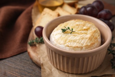 Photo of Tasty baked camembert in bowl on wooden table, closeup. Space for text