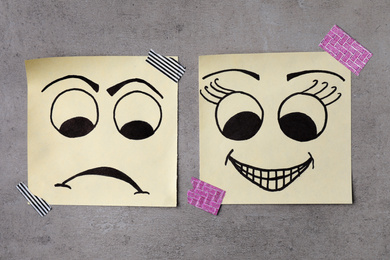 Photo of Paper notes with drawn faces on grey background, flat lay. Concept of jealousy