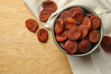 Photo of Tasty apricots with bowl on wooden table, flat lay and space for text. Dried fruits
