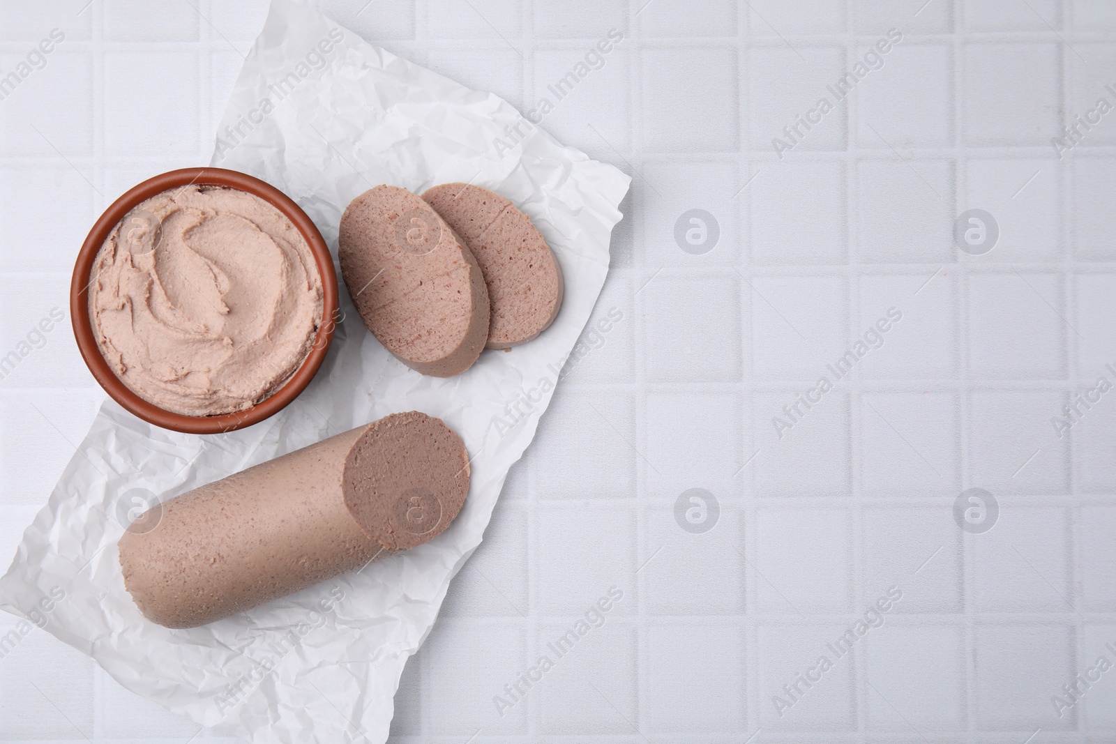 Photo of Delicious liver sausage and paste on white tiled table, flat lay. Space for text