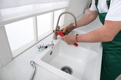 Professional plumber fixing water tap in kitchen, closeup