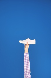 Photo of Young woman holding comfortable shoe on blue background, closeup