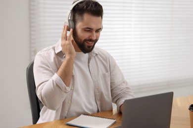 Young man in headphones watching webinar at table in room