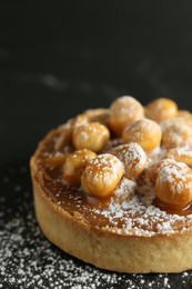 Delicious tart with hazelnuts, sweet caramel and powdered sugar on black table, closeup