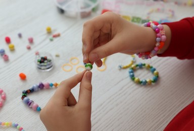 Photo of Girl making beaded jewelry at white wooden table, closeup