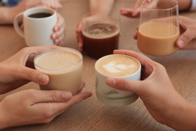 Friends drinking coffee at wooden table in cafe, closeup