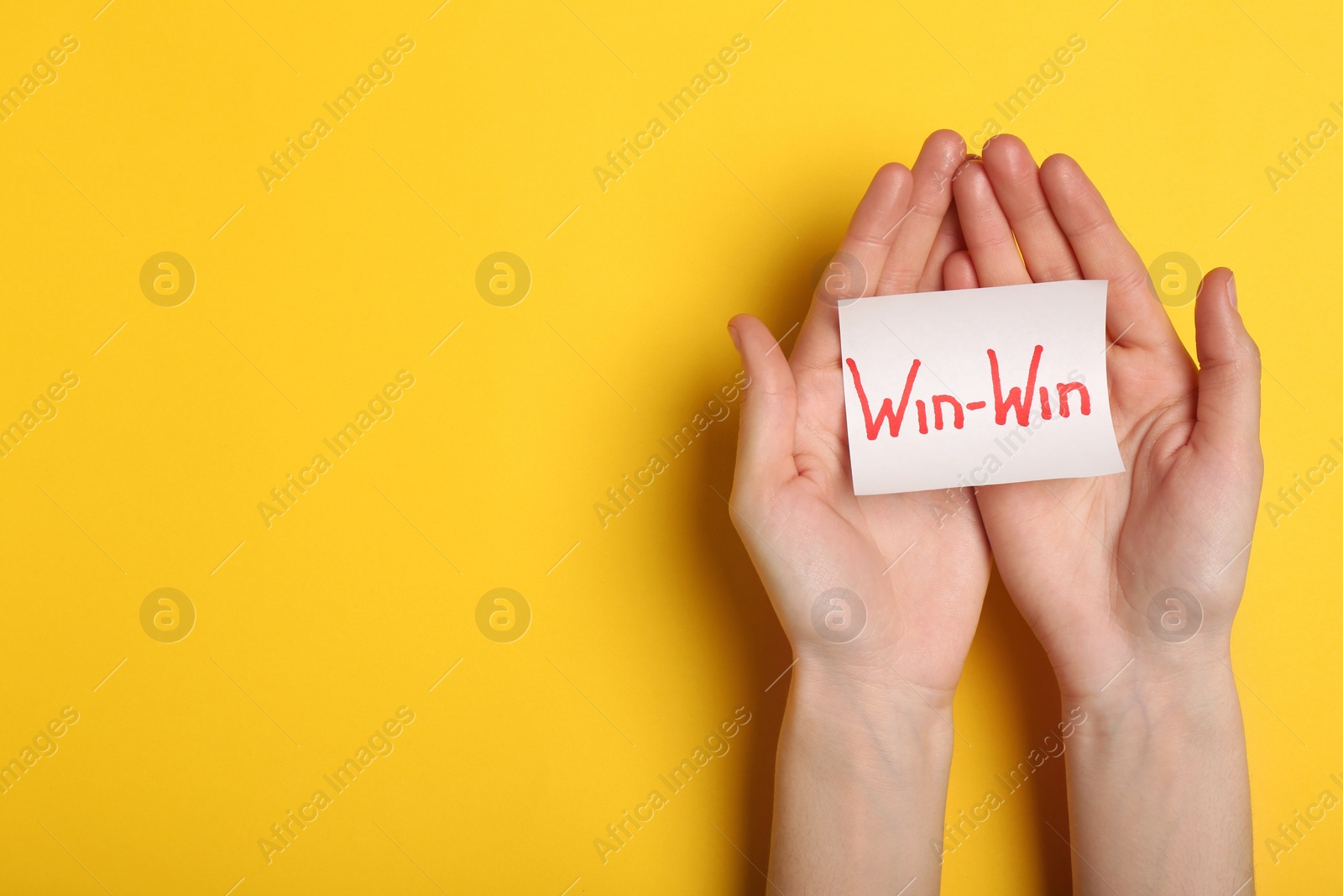 Photo of Top view of woman holding paper card with words WIN-WIN on color background, space for text. Victory concept
