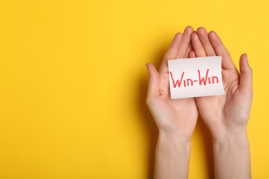 Photo of Top view of woman holding paper card with words WIN-WIN on color background, space for text. Victory concept