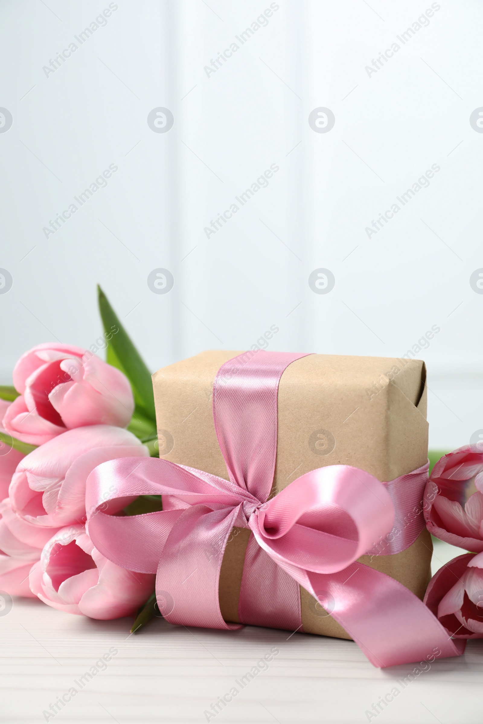 Photo of Beautiful gift box with bow and pink tulips on white table. Space for text