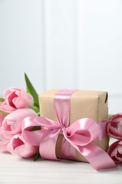 Beautiful gift box with bow and pink tulips on white table. Space for text