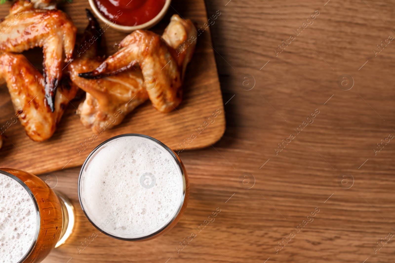 Photo of Glasses with beer and delicious baked chicken wings on wooden table, flat lay. Space for text