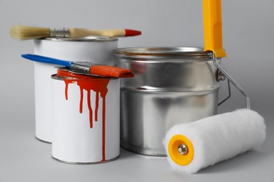 Photo of Cans of orange paint, brushes and roller on grey background
