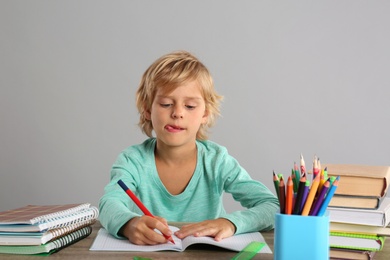 Little boy doing homework at table on grey background