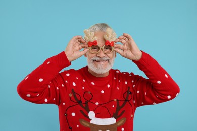 Happy senior man in Christmas sweater and party glasses on light blue background