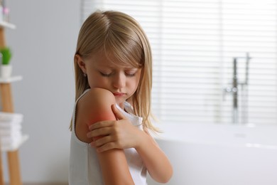 Photo of Suffering from allergy. Little girl scratching her arm in bathroom, space for text