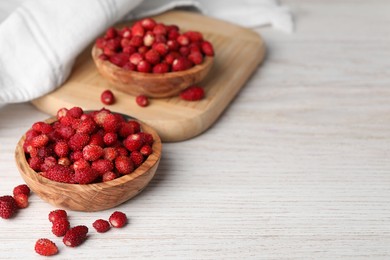 Photo of Fresh wild strawberries in bowls on white wooden table. Space for text