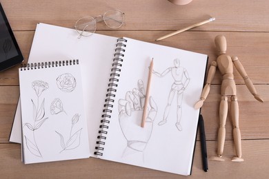 Photo of Sketchbook with beautiful drawings, mannequin and pencils on wooden table, flat lay