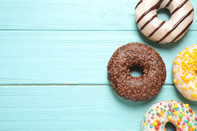 Photo of Delicious glazed donuts on blue wooden table, flat lay. Space for text