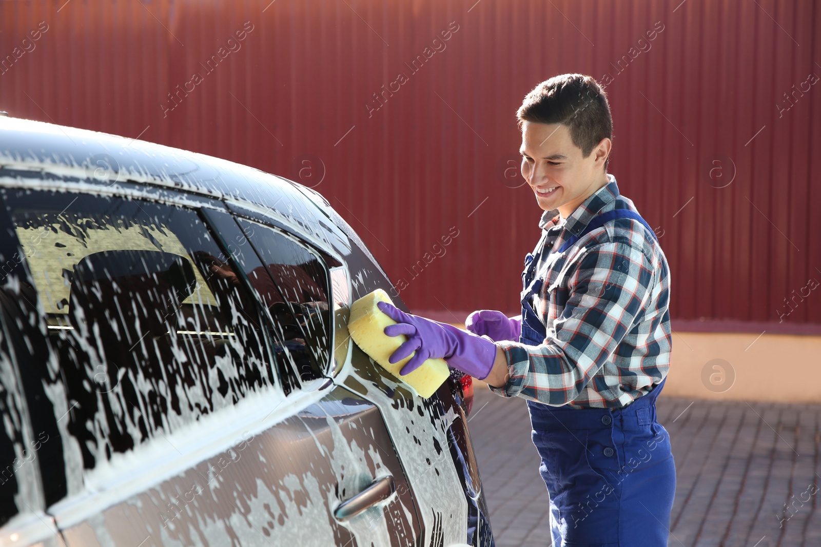 Photo of Worker cleaning automobile with sponge at car wash