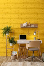 Photo of Modern workplace interior with wooden furniture and laptop near yellow brick wall