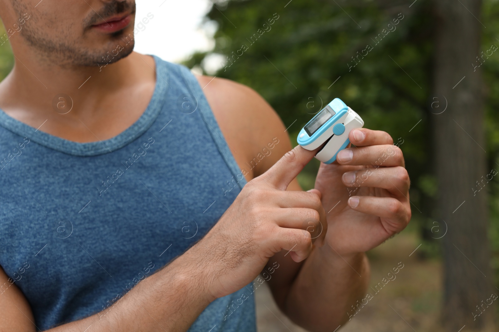 Photo of Young man checking pulse with medical device after training in park, closeup