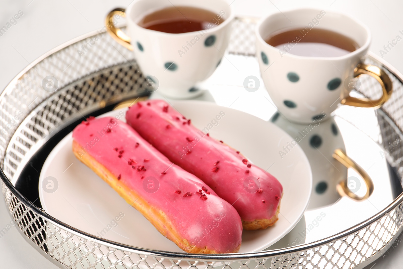 Photo of Tray with tasty glazed eclairs and tea on white table, closeup