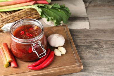 Tasty rhubarb sauce and ingredients on wooden table, space for text