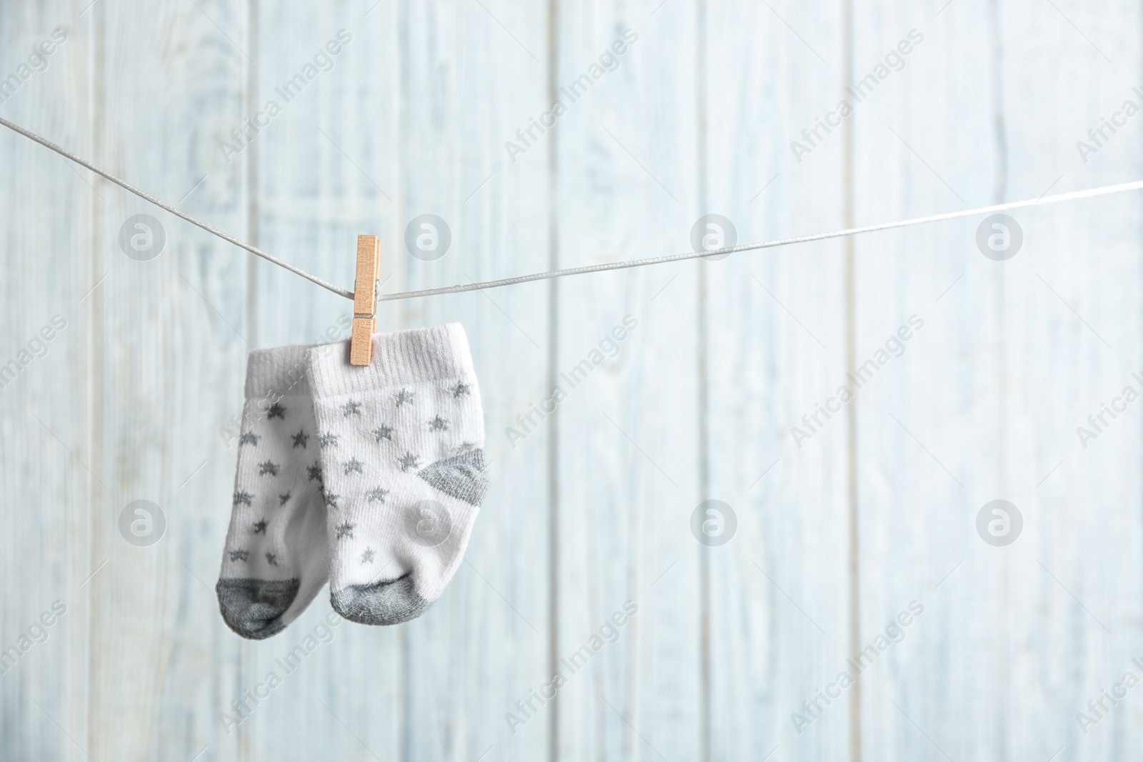 Photo of Pair of socks on laundry line against wooden background, space for text. Baby accessories