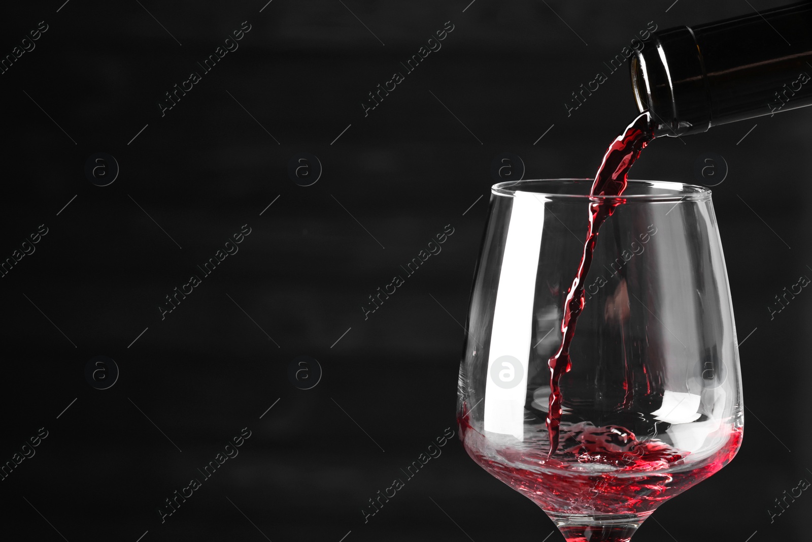 Photo of Pouring red wine into glass against dark background, closeup. Space for text