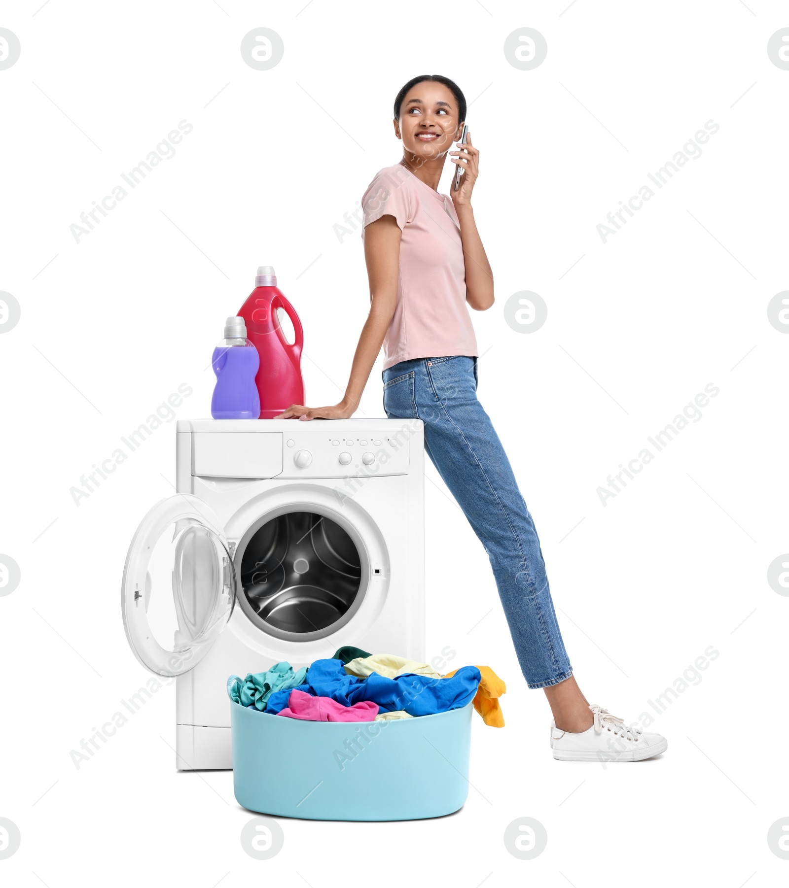 Photo of Beautiful woman talking on phone near washing machine with laundry against white background