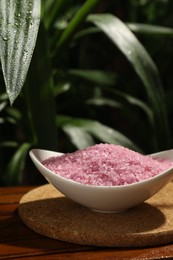 Photo of Bowl of pink sea salt on wooden table, closeup. Space for text