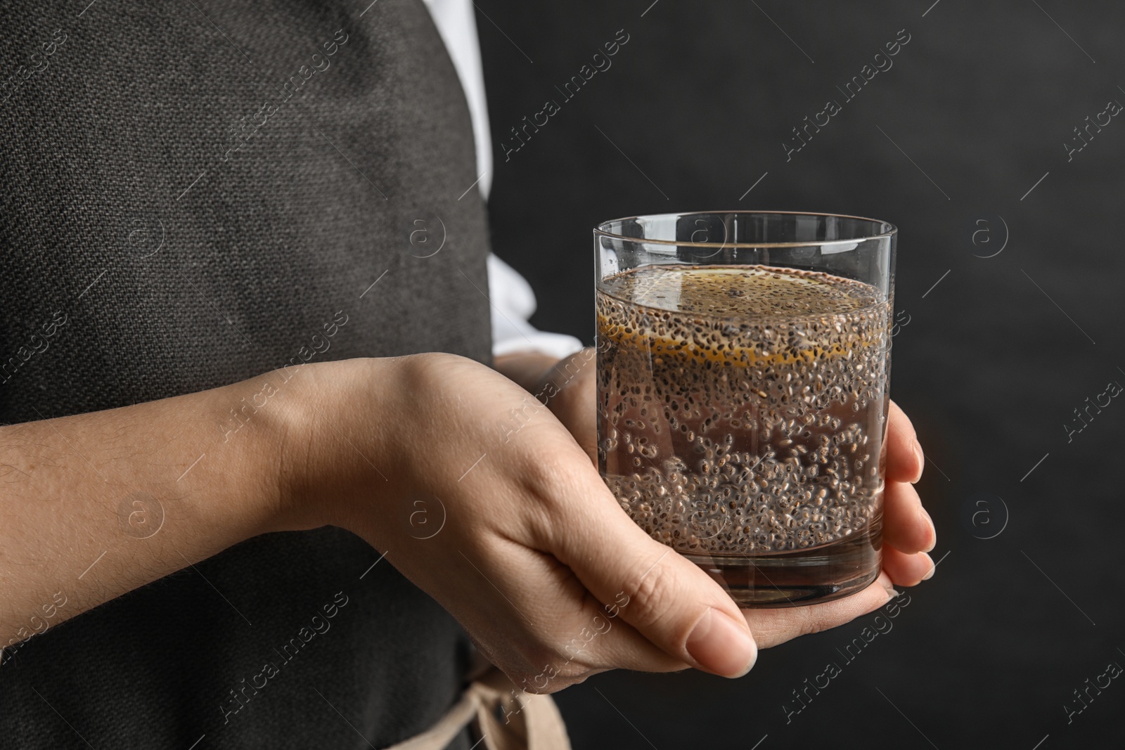 Photo of Woman holding glass of water with chia seeds on black background, closeup