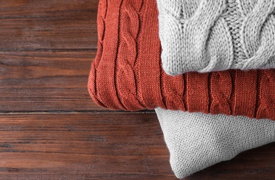 Stack of folded warm sweaters on wooden background, closeup