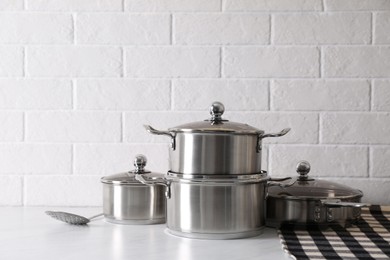 Photo of Set of stainless steel cookware on table near white brick wall