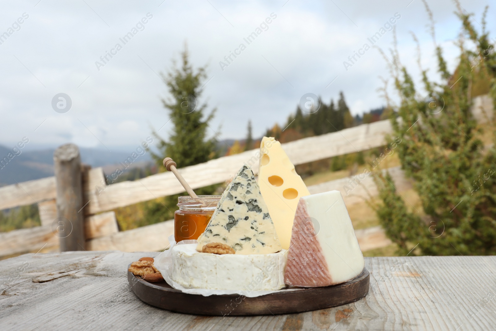 Photo of Different types of delicious cheeses on wooden table against mountain landscape