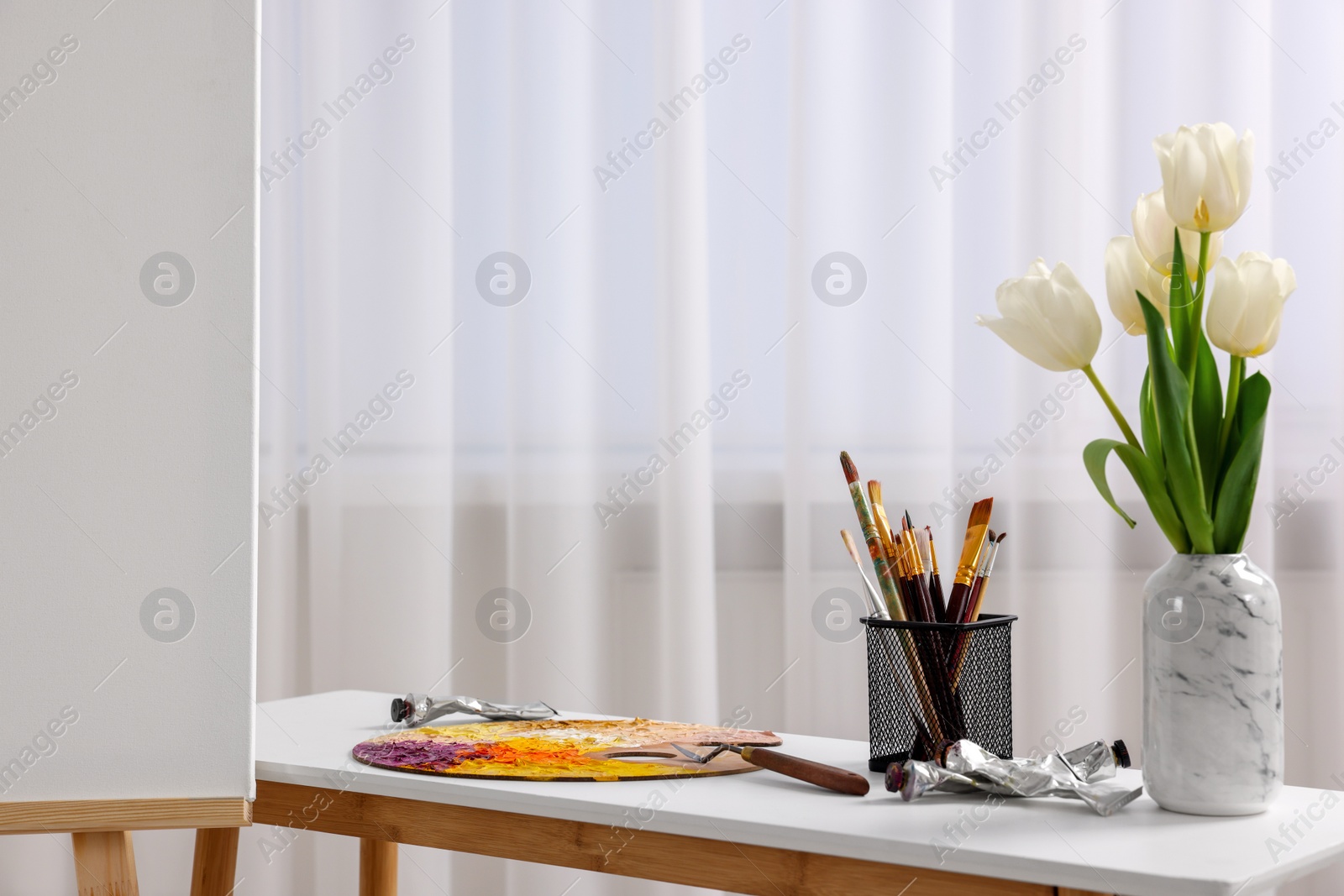 Photo of Wooden easel with canvas and art supplies on table indoors. Space for text