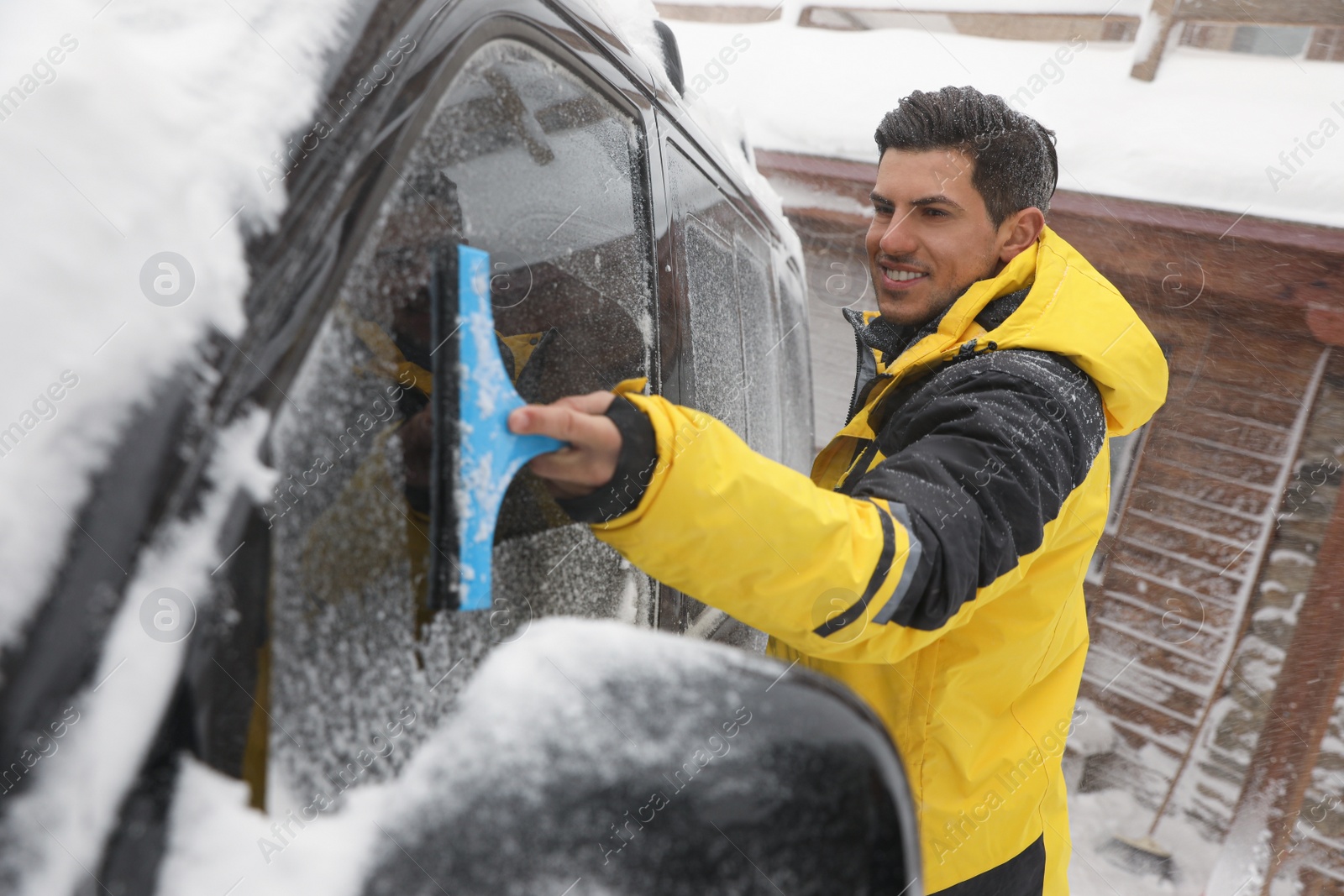 Photo of Man cleaning snow from car window outdoors on winter day