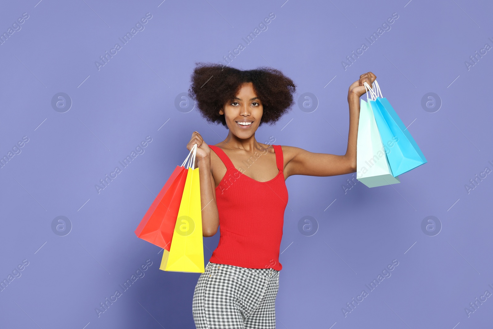 Photo of Happy African American woman with shopping bags on purple background