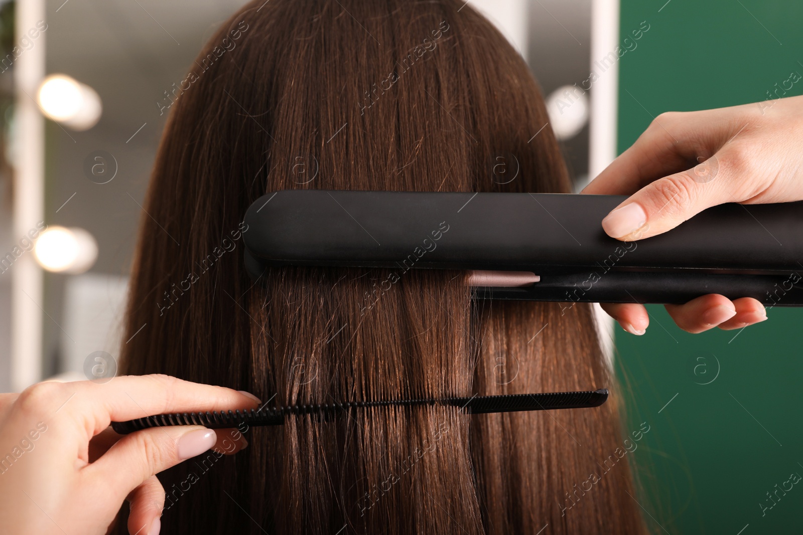 Photo of Stylist straightening woman's hair with flat iron in salon