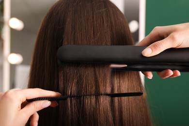 Photo of Stylist straightening woman's hair with flat iron in salon