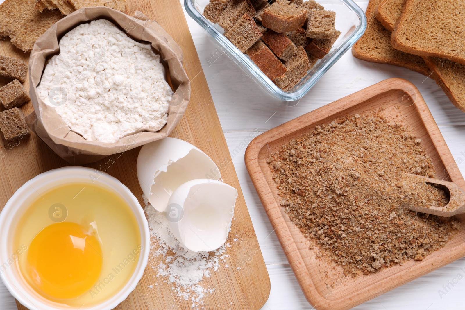 Photo of Fresh breadcrumbs, flour and egg on white wooden table, flat lay