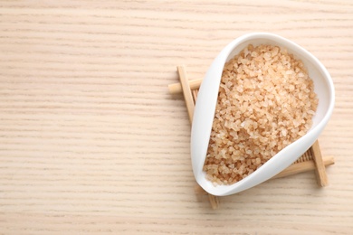 Photo of Bowl of brown sea salt on wooden table, top view with space for text. Spa treatment