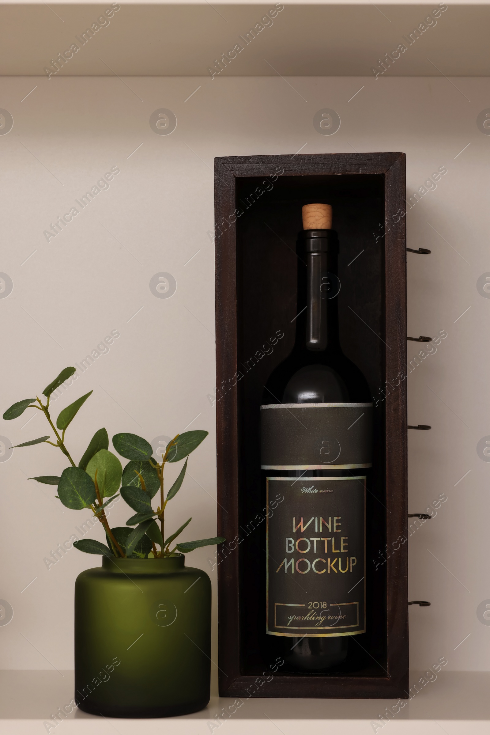 Photo of Shelf with houseplant and wine bottle near beige wall. Interior design