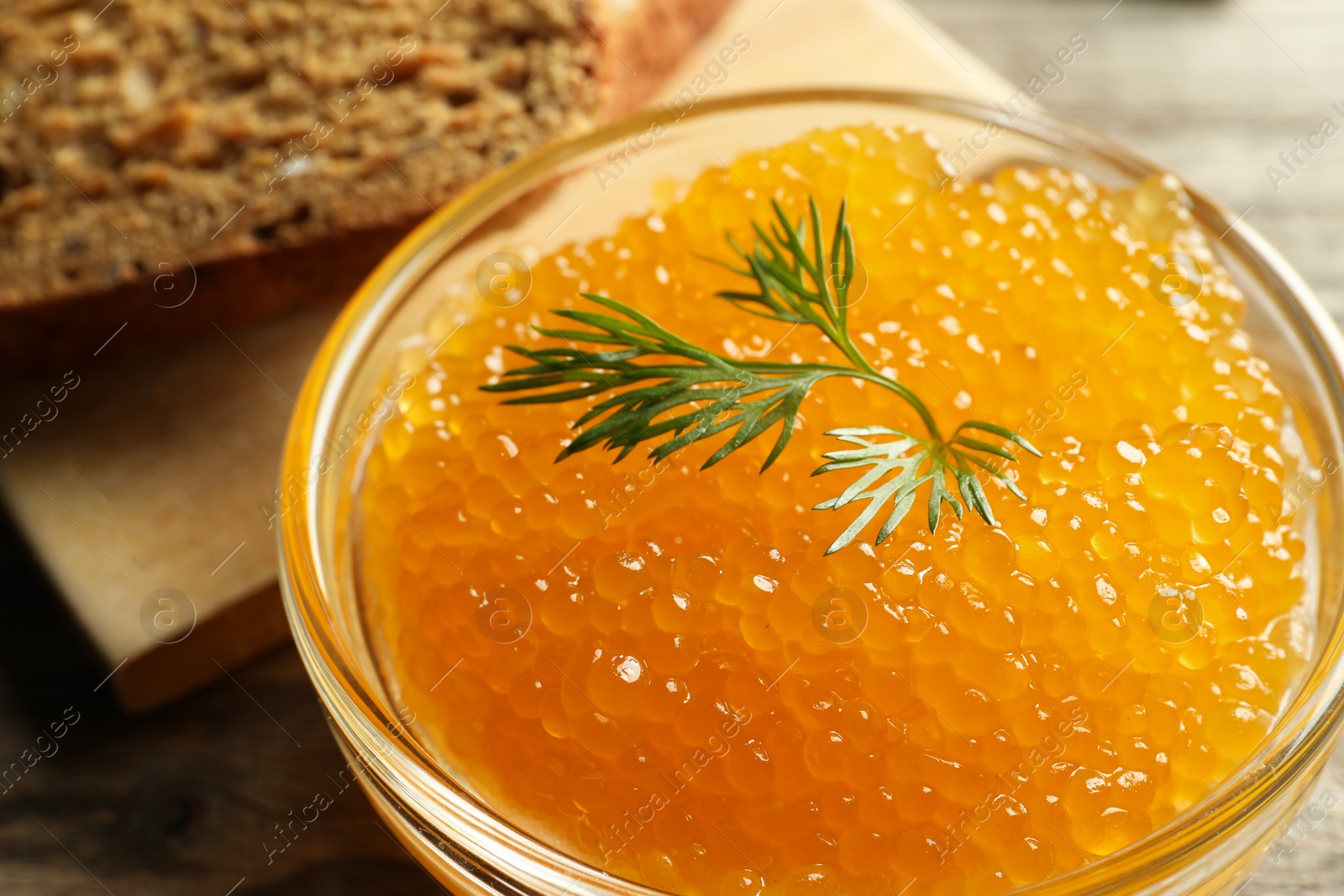 Photo of Fresh pike caviar in bowl and bread on wooden table, closeup