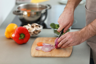 Photo of Young man cutting vegetables for soup in kitchen, closeup