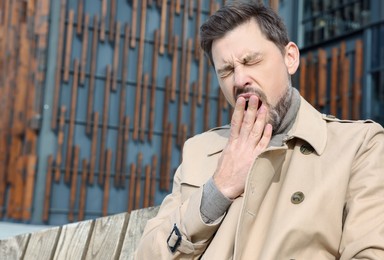 Photo of Sleepy man yawning on wooden bench outdoors. Space for text