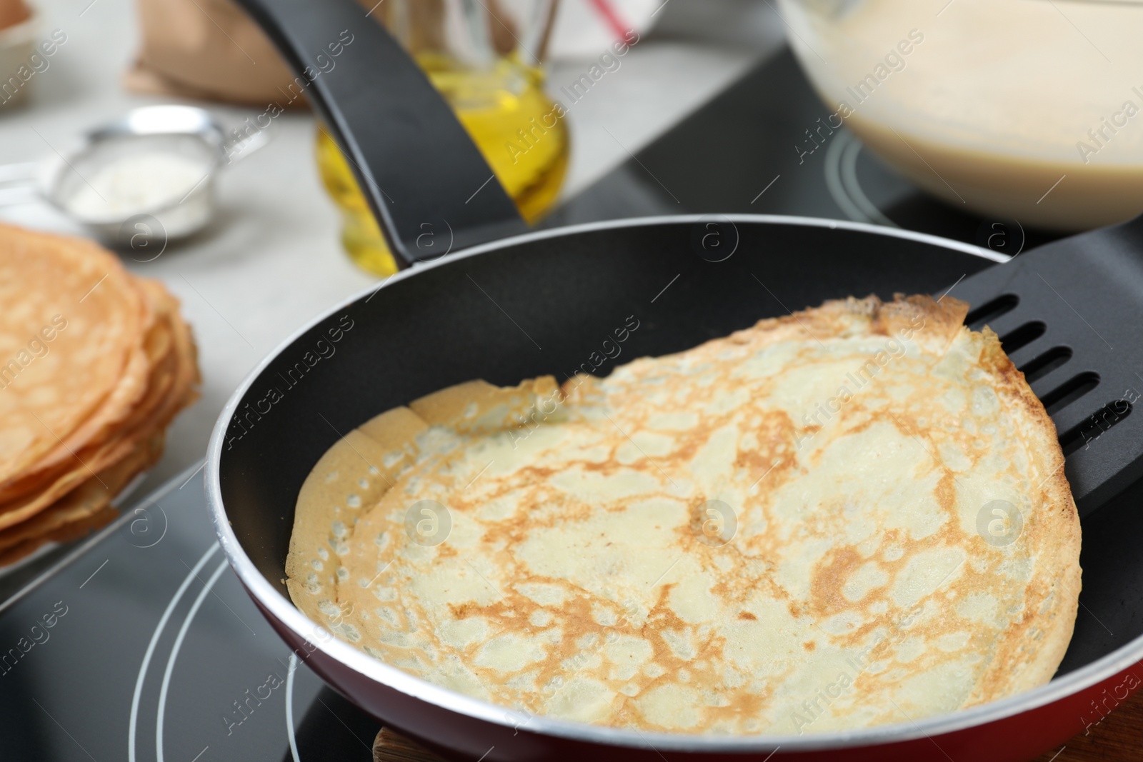 Photo of Delicious thin pancake in frying pan on induction stove, closeup