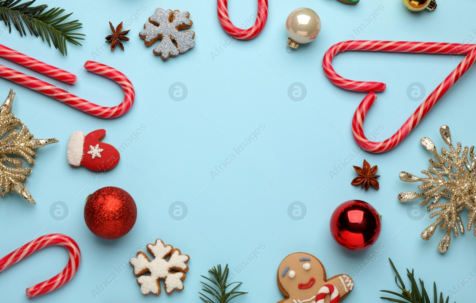 Photo of Frame of sweet candy canes and Christmas decor on light blue background, flat lay. Space for text