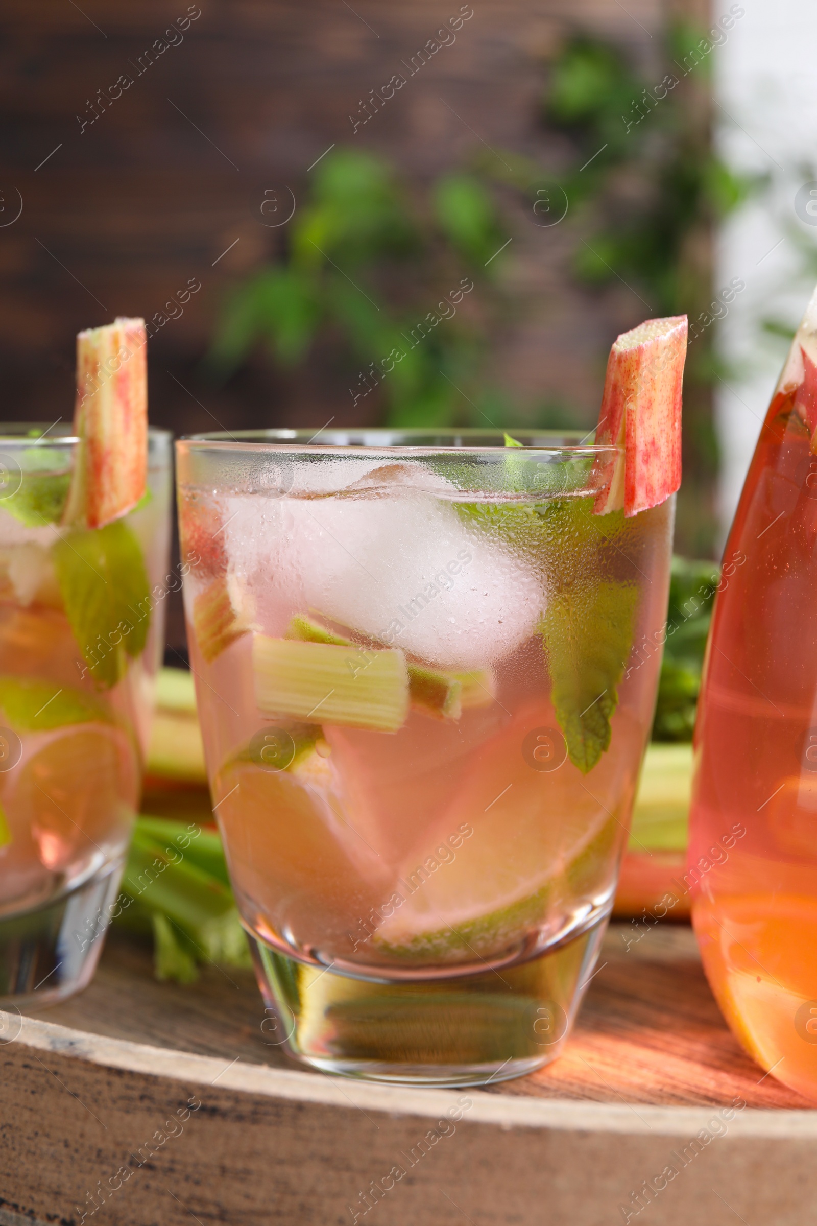 Photo of Glasses of tasty rhubarb cocktail with lime fruits on wooden board, closeup